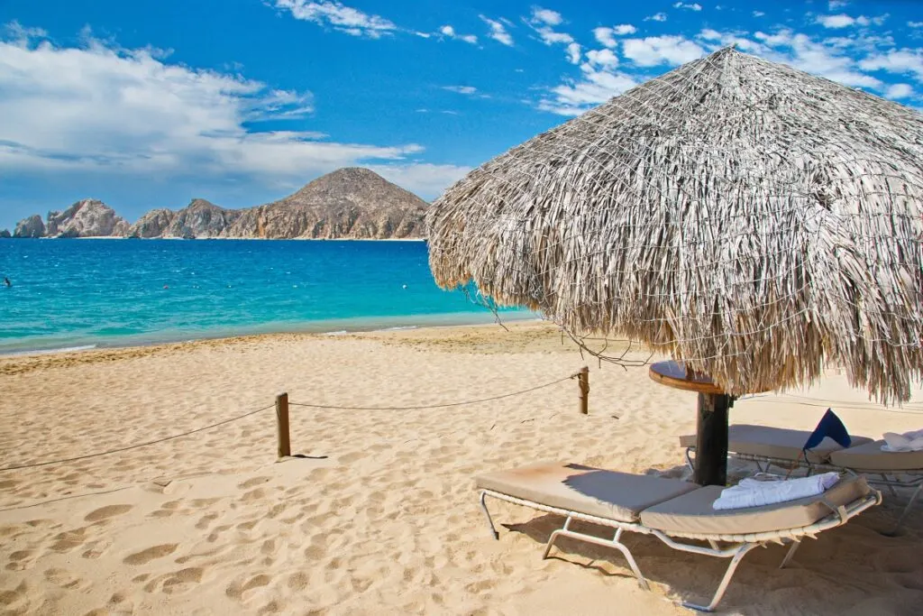 Beach location with chaise and umbrella for relaxation in Cabo San Lucas, Mexico with mountains in view across the water.