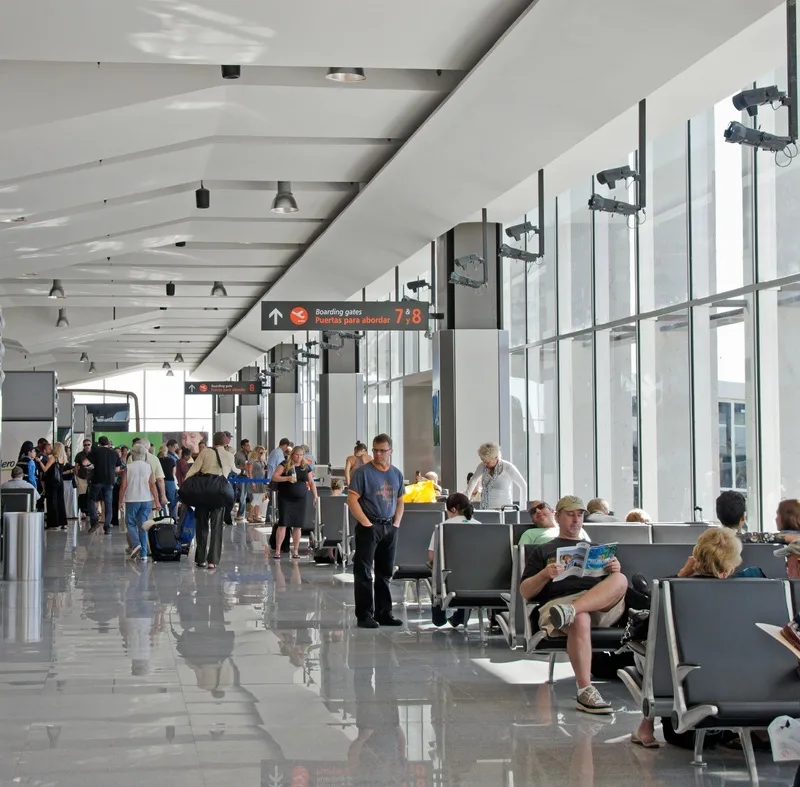 Los Cabos International Airport gate with tourists waiting for their flights, standing with luggage, reading a magazine, and resting.