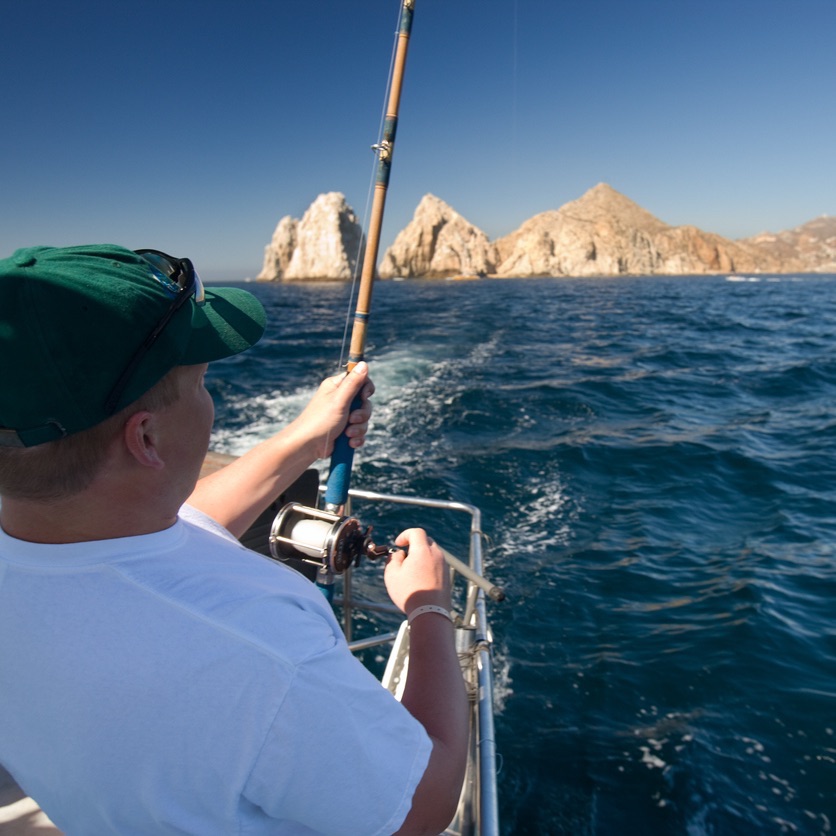 Man deep sea fishing, standing at end of boat with fishing rod fighting Cabo San Lucas