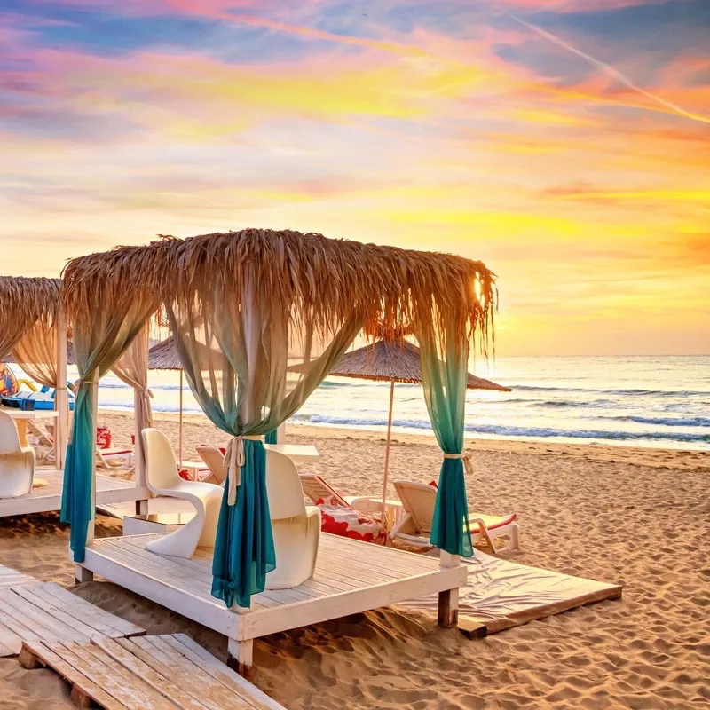 Coastal landscape at sunrise - view of the sandy seashore with beach gazebos. Beach holiday concept