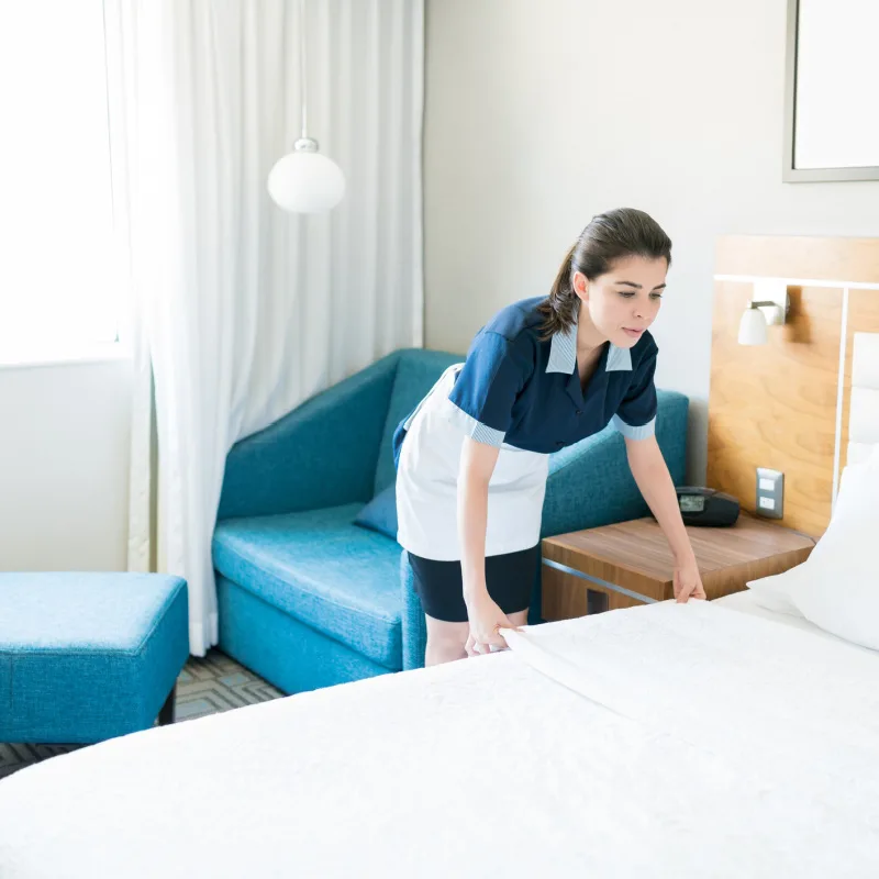 Mid adult Latin housekeeper setting white sheet on bed in hotel room