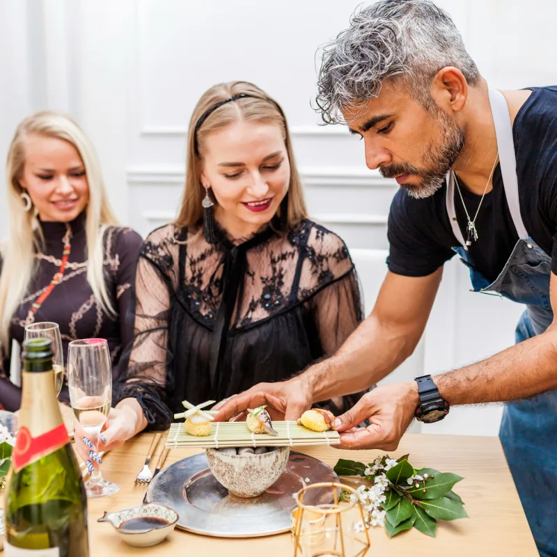 Latin cook serving food to clients at table during private dinner at home. Chef serving sushi to stylish group of people.