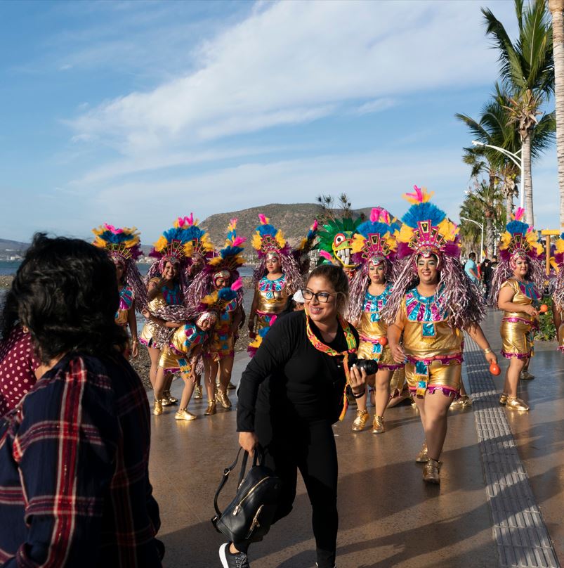 Tourists walking near ocean and traditional dancers in gold costumes