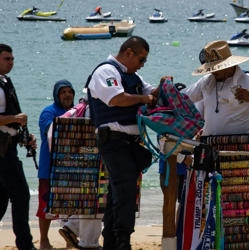 Mexico police searching a beach vendor with bracelets and banners