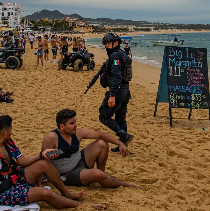 Mexican police looking back at two men sitting on the beach