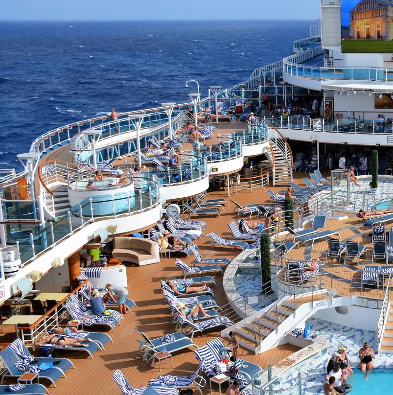 Cruise ship deck with many sunbeds, a pool, television and hot tubs