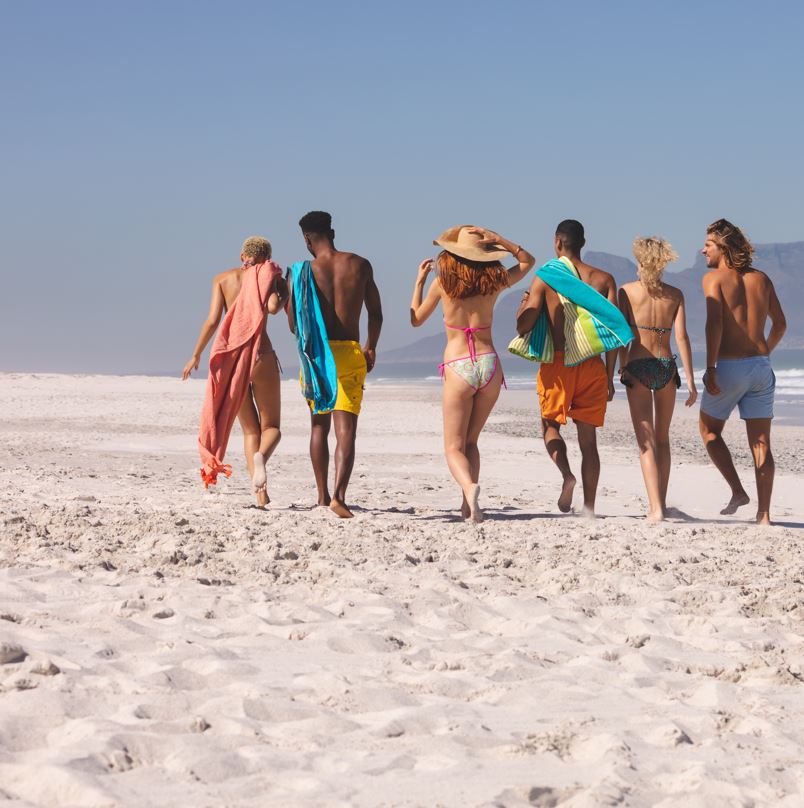 Group of friends walking on the sand near the ocean