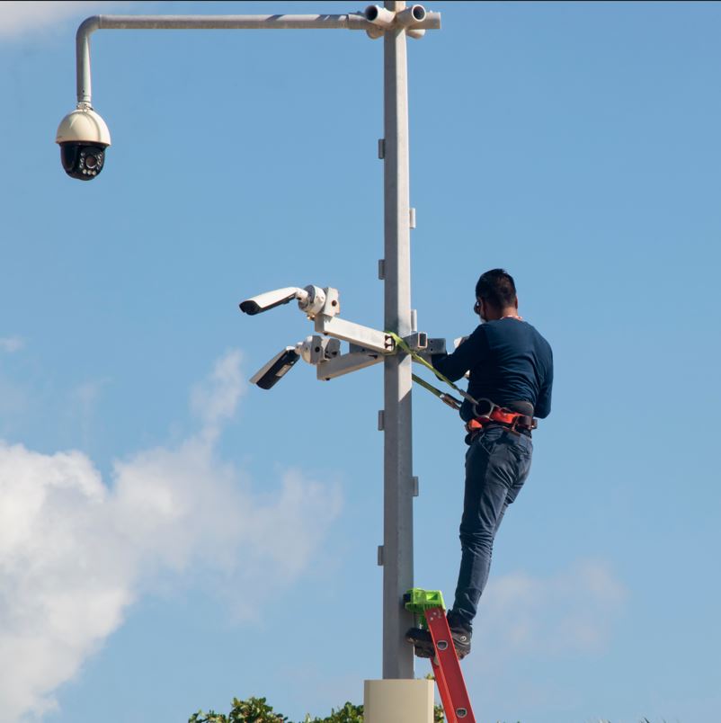Technician installing security cameras near palm trees