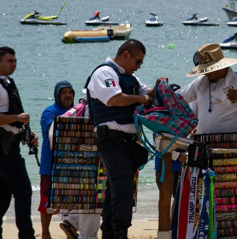Police on beach inspecting a seller with jewellery and souvenirs
