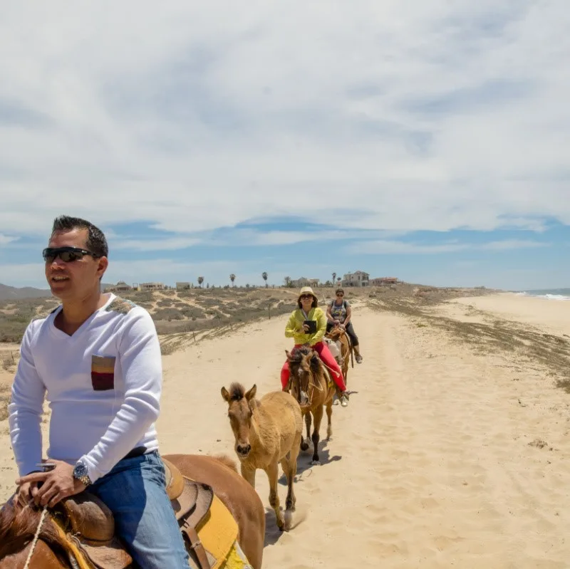 Horseback Riding on a beach in Los Cabos with a view of the sea in the distance.