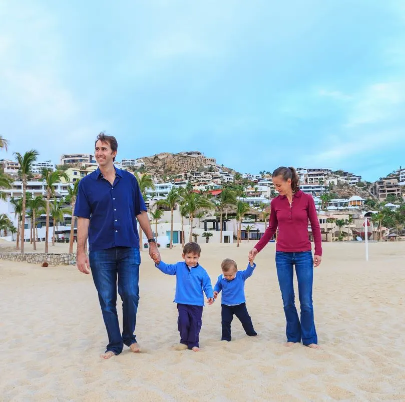 Young Family Enjoying Cabo Beach with resorts in the background.