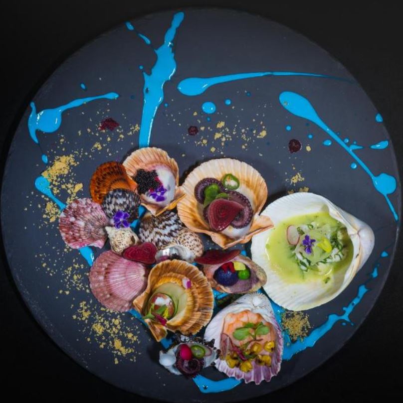 Black plate filled with seafood decorated with flowers and colorful sauces