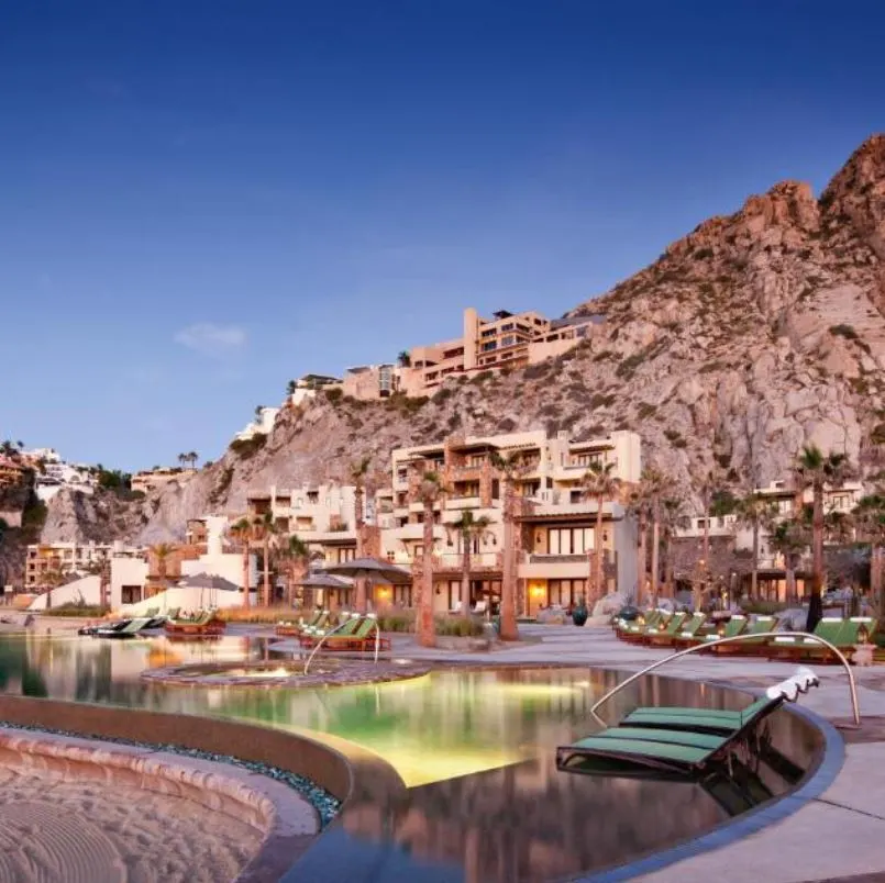 Beautiful Cabo beachfront resort with a pool and lounge chairs next to a sandy beach.