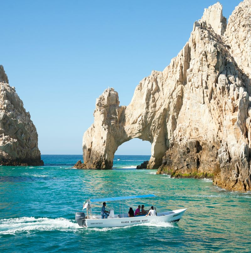 Tourists on a glass bottom boat in front of the Los Cabos arch in Mexico