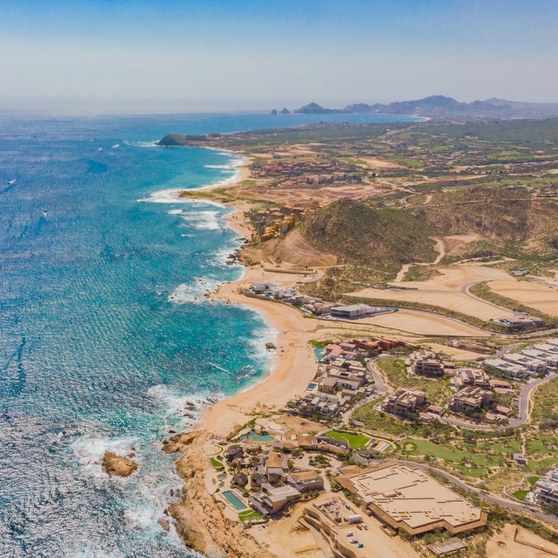 Aerial View of San Jose del Cabo coastline with water, sand, and buildings below.