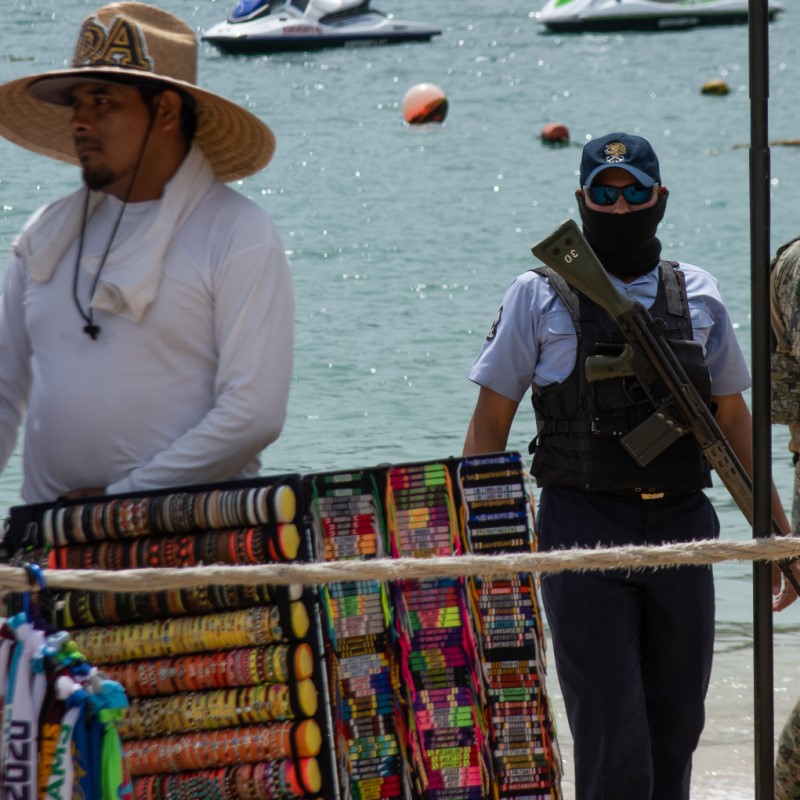 Armed Guard at Cabo Beach with a vendor standing in view and the water in the background.