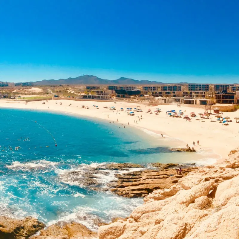 Busy Santa Maria Beach in Cabo with beautiful aqua blue water and hills in the background.