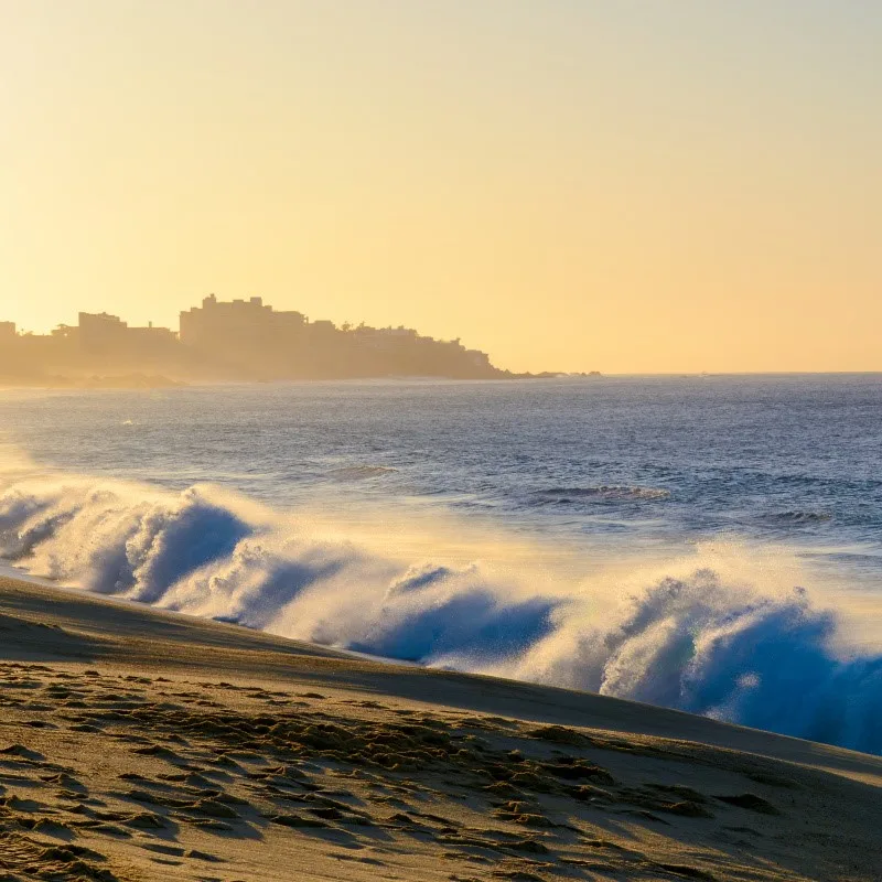 Cabo San Lucas Beach with sand and strong waves, looking out at the sea.