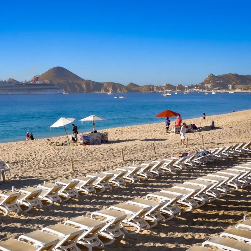 Chairs and Vendors on Medano Beach with a view of the water and the famous Cabo San Lucas Arch in the background.