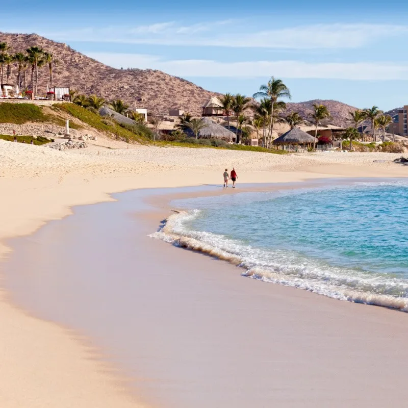 Couple Walking on the Beach in Cabo San Lucas with hills in the background.