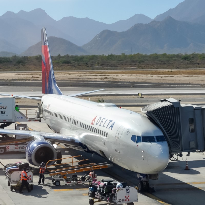 Delta Plane in Cabo waiting on the tarmac, with people and airport vehicles around.