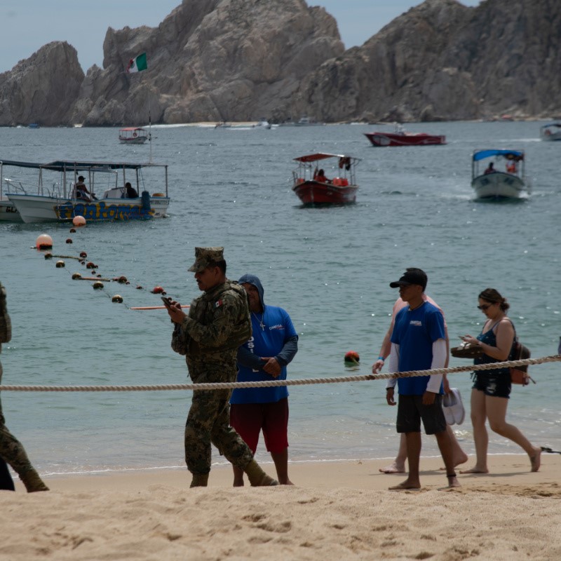 Guard on the Beach in Cabo with tourists walking around and boats in the water.