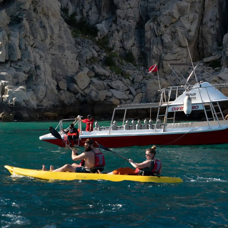 Tourists enjoying Los Cabos Activities, kayaking and diving, on a warm day with Land's End in the background.