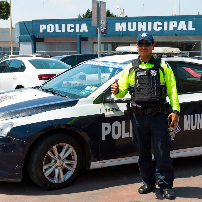 Municipal Mexican cop stands beside patrol car