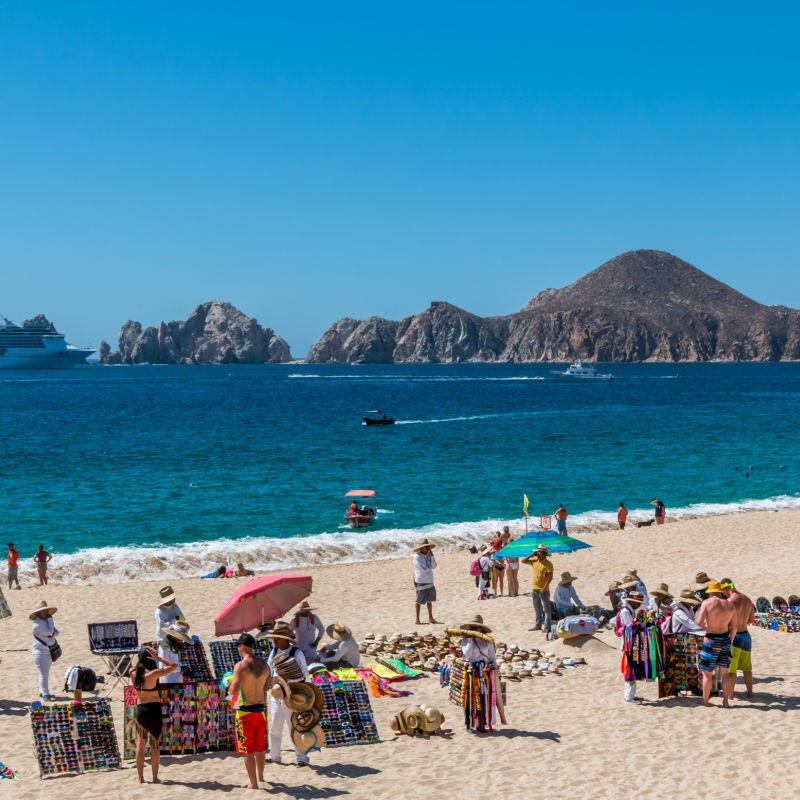 Busy Cabo Beach with vendors and people everywhere and Land's End in the background.