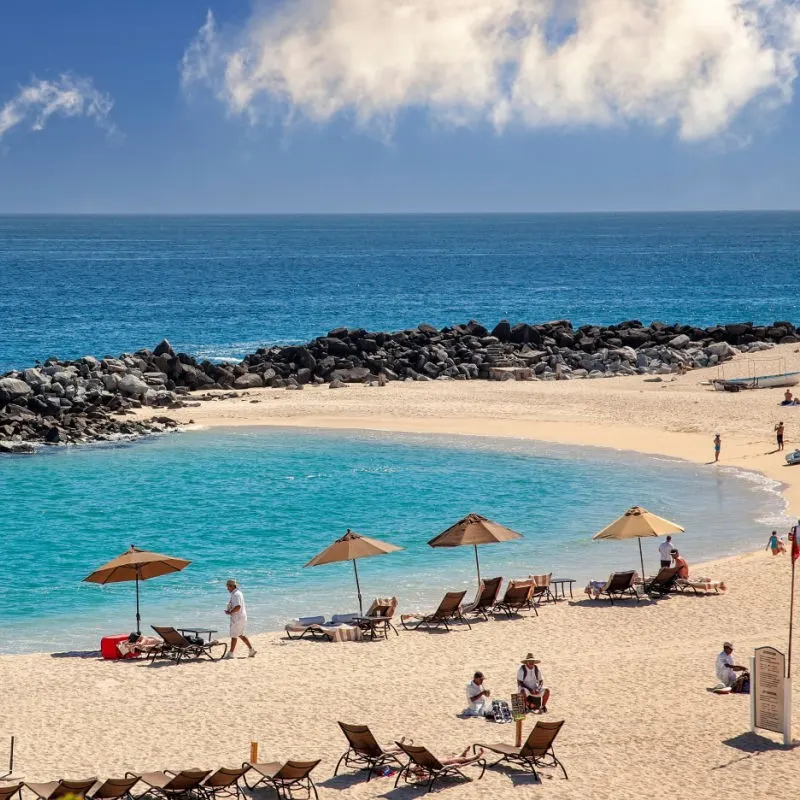 Tourists on a Cabo Beach with chairs and umbrellas set up and a red flag off to the right barely visible.