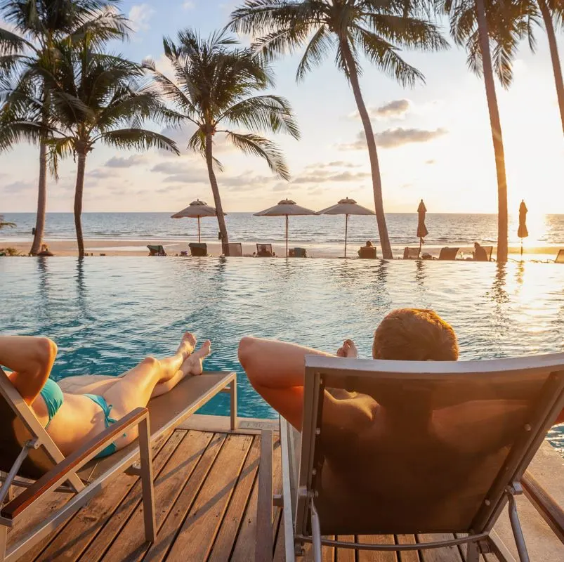 Travelers in a lounge chair at a pool in tropic setting