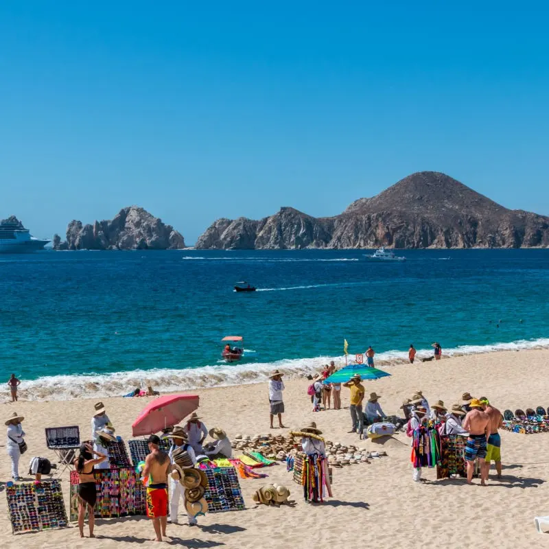 Vendors on Cabo Beach with the famous Arch of Cabo San Lucas in the background.