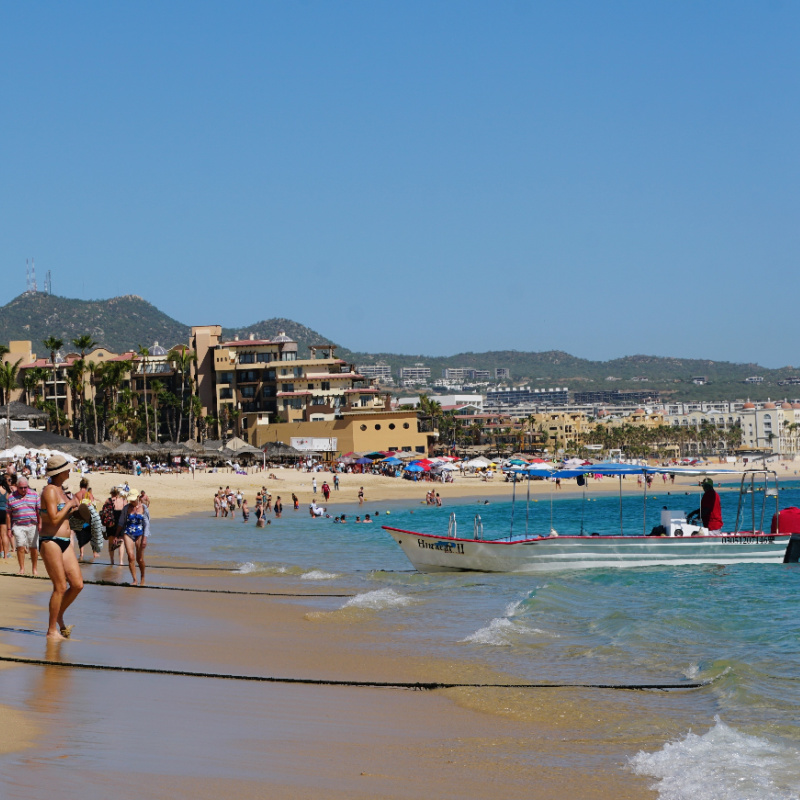 Tourists walking along busy Los Cabos beaches with a boat nearby