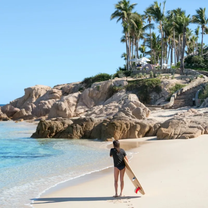 Girl on a Beach in Los Cabos with a Surfboard Looking Out at the Water