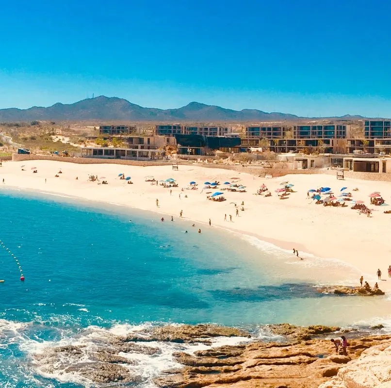 Los Cabos beach with people enjoying the ocean and a resort in the background