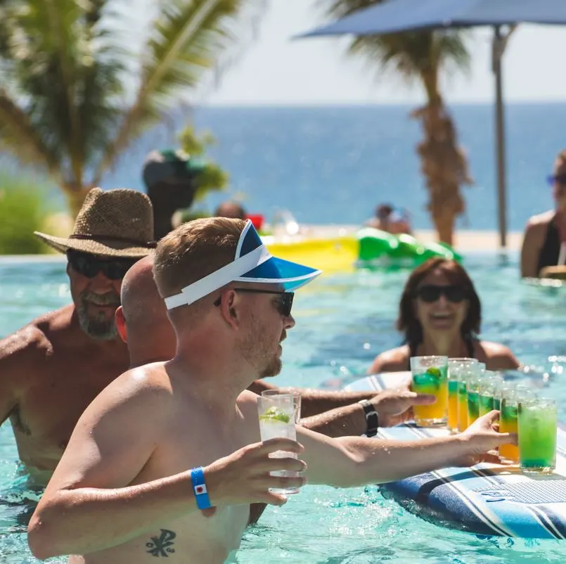 People playing in a Cabo pool with a surf board full of drinks