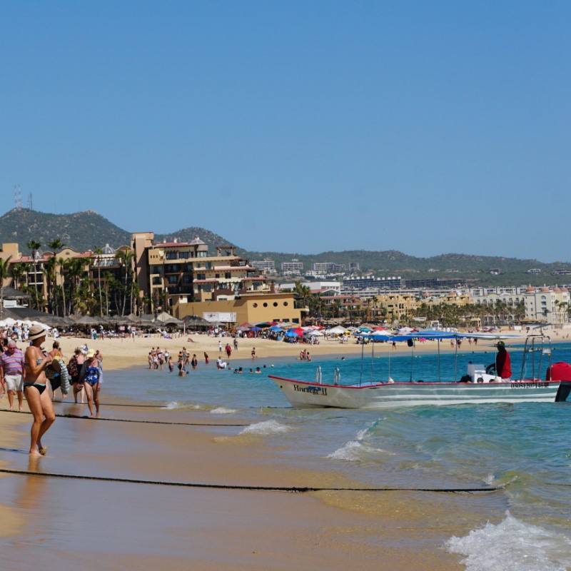 Tourists on a Beach in Cabo San Lucas with a Boat and Resorts in the Background