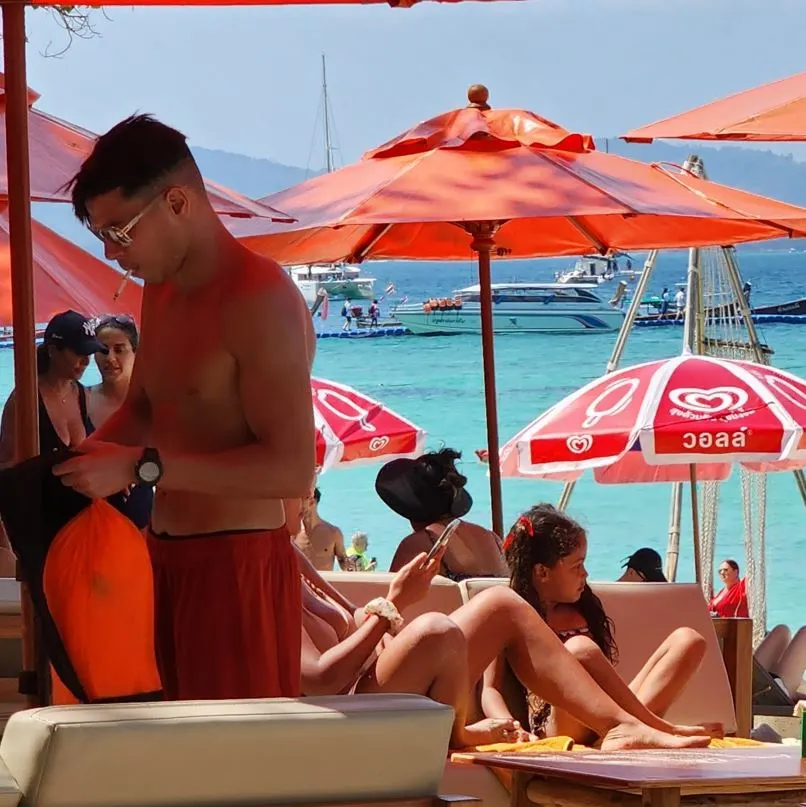 People At A Beach Club With Boats In The Background