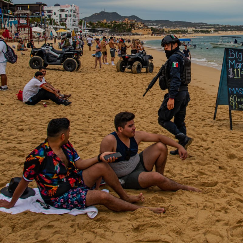 Police Officer Walking Past Tourists on a Cabo San Lucas Beach
