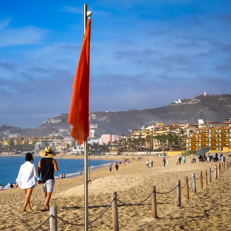 Red Flag and Tourists on Medano Beach in Cabo San Lucas, Mexico