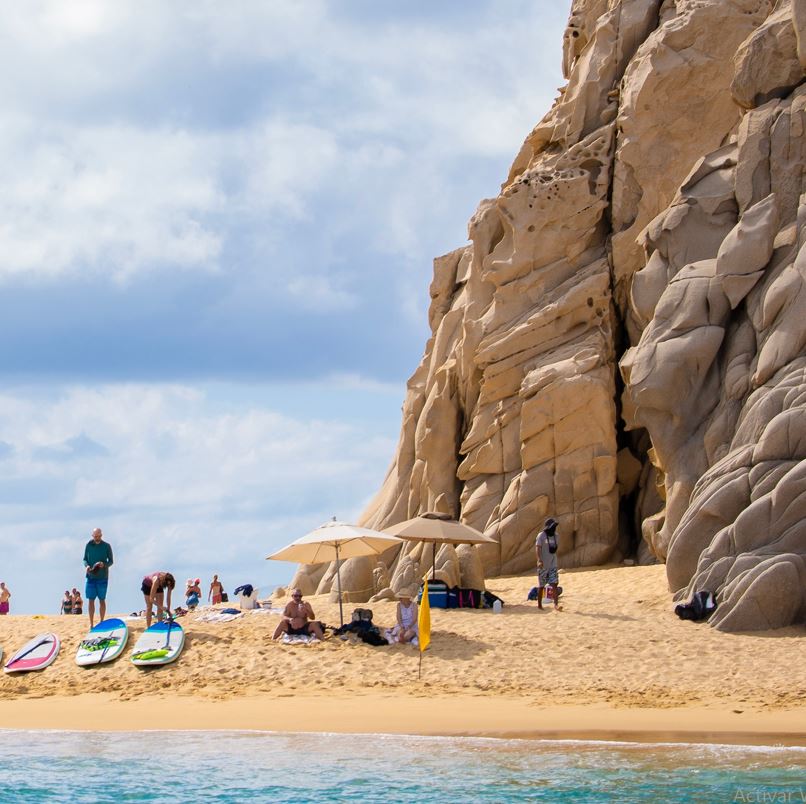 People With Kayaks In A Beach Between Two Rocks In Los Cabos