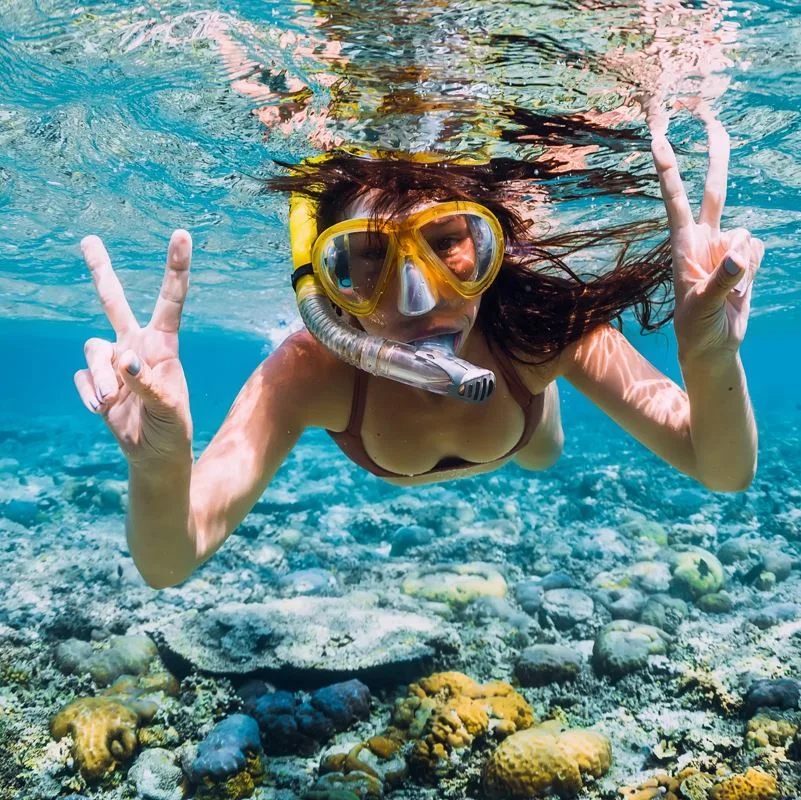 A snorkeler in the pacific ocean making the peace symbol with her hands