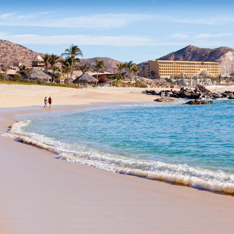 Couple Walking Along a Los Cabos Beach Past Strong Waves