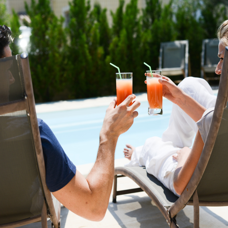 A couple toasting cocktails by a pool