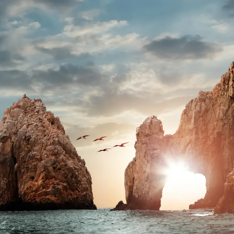 storm clouds and the sun shining on the los cabos arch