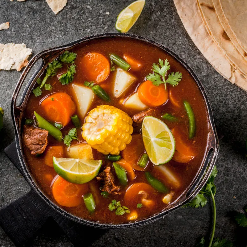 Mexican traditional vegetable soup Mole de olla with meat, potatoes, carrots, beans, corn and lime
