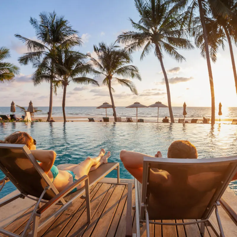 travelers relaxing by their resort poolside at sundown