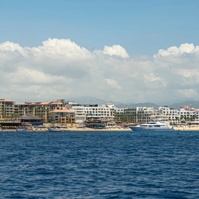 Panoramic view of the bay of Cabo San Lucas on a sunny summer afternoon with hotels and mountains in the background, turquoise sea and blue sky with clouds