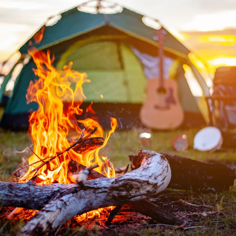 tent in a natural area with campfire in the front and a guitar in the background