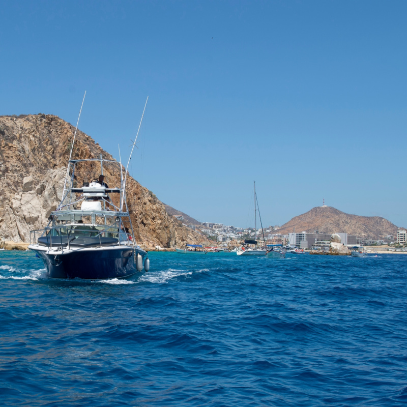 Black yacht leaving the bay of Cabo San Lucas near Lovers Beach the south of Baja California peninsula, with clear blue sky and mountains in the background. sailing on the turquise blue sea of cortes